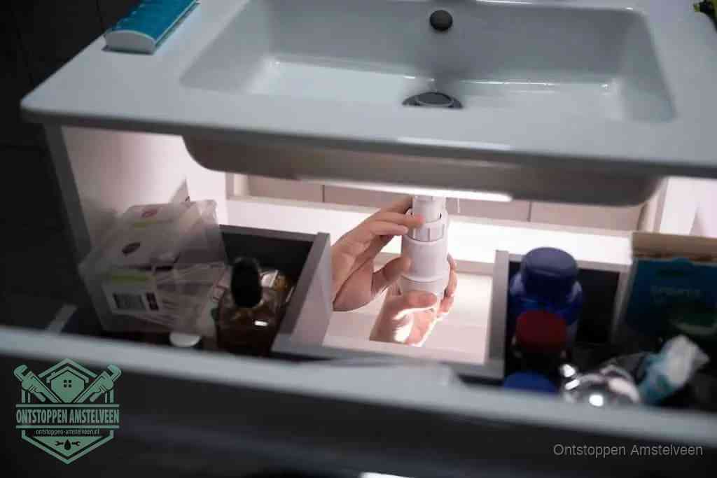 Een pompfles met zeep boven een wastafel, de heet water en afwasmiddel-methode om een vetprop in de afvoer los te maken in Amstelveen
