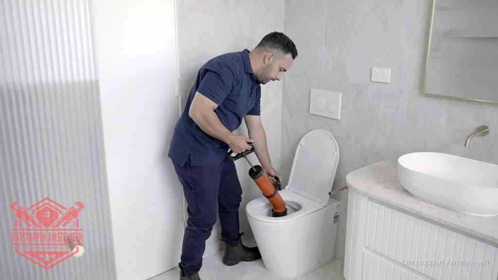 Een monteur buigt over een wandcloset en duwt met de hand een persluchtontstopper in de toiletpot om de verstopping handmatig los te maken in Amstelveen