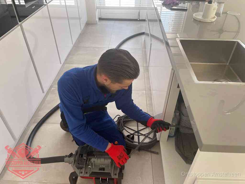 Een monteur ontstopt de keukenafvoer onder de spoelbak met een elektrische veermachine in Amstelveen