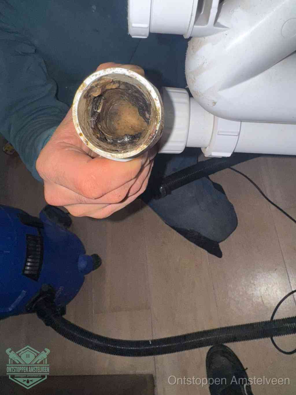 Een hand houdt een losgekoppeld PVC-afvoerbuisstuk vast dat van binnen volledig is dichtgeslibd met vet, vuil en aanslag, de meest voorkomende oorzaak van een verstopte afvoer in Amstelveen