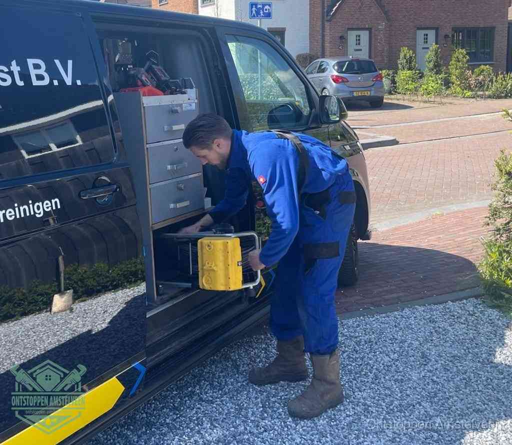 Een monteur pakt buiten op de oprit gereedschap uit de bedrijfsbus, het moment om een professional in te schakelen voor een verstopte afvoer in Amstelveen
