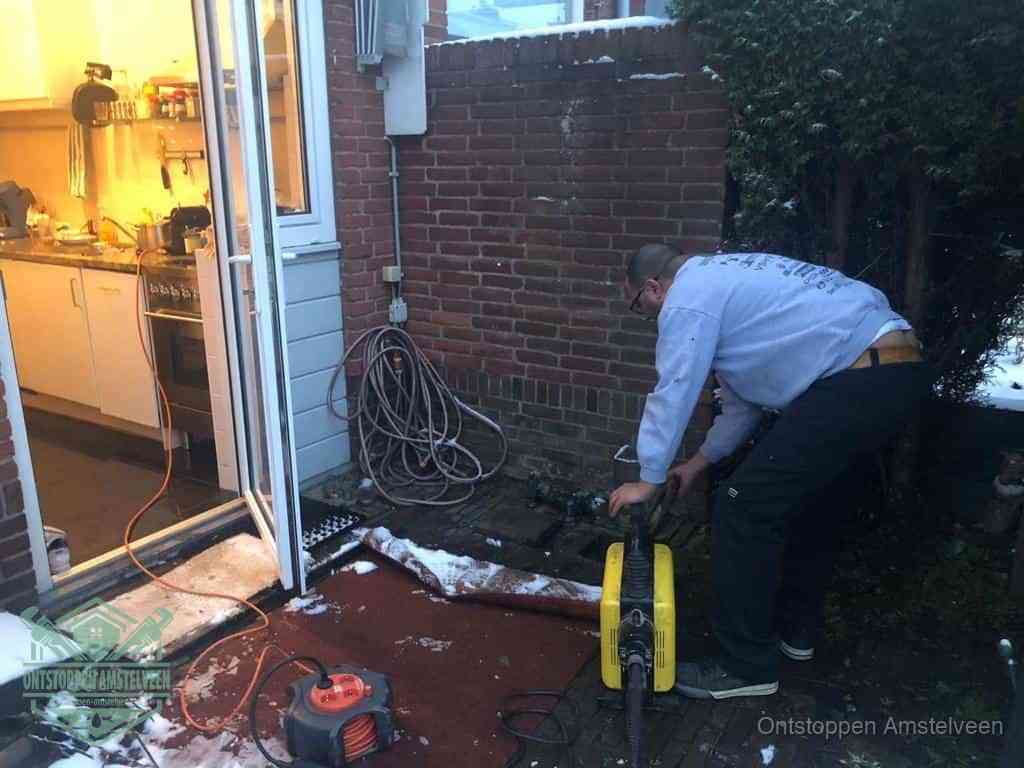 Een monteur werkt buiten bij een open riool-/grondput met een elektrische ontstoppingsmachine om een verborgen afvoerprobleem op te sporen in Amstelveen