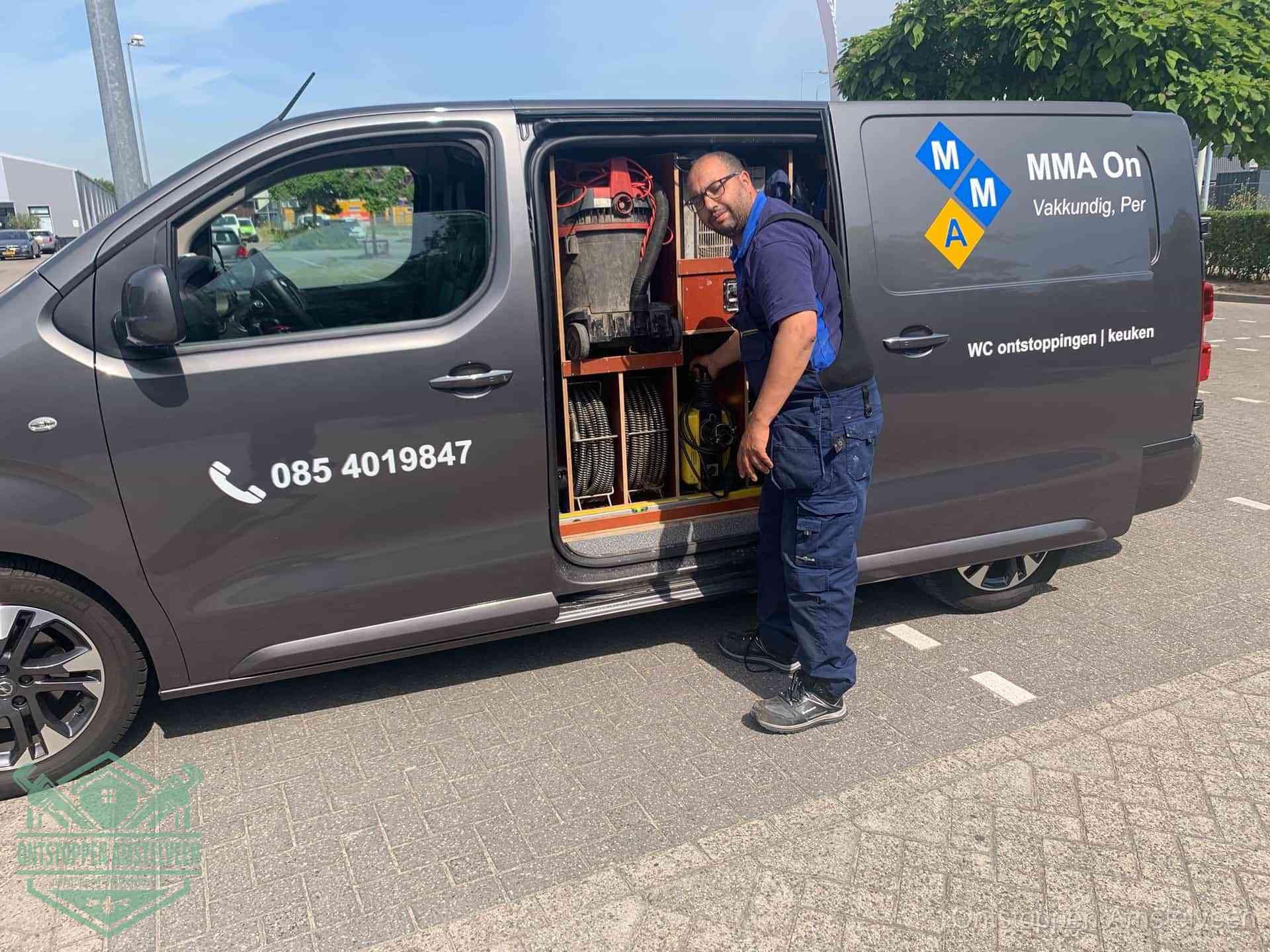 Een monteur bij de open schuifdeur van zijn bedrijfsbus op een parkeerplaats, klaar om de oorzaak van terugkerende afvoerverstoppingen aan te pakken in Amstelveen