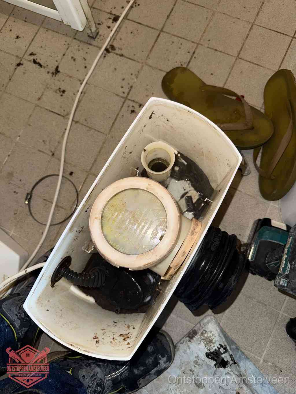 Een gedemonteerde toiletpot op de vloer met ontstoppingsveer en gereedschap ernaast, het verwijderen van een vastzittend voorwerp uit de wc in Amstelveen