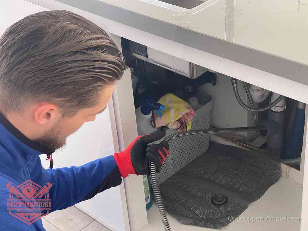 Een monteur voert een flexibele ontstoppingsveer in de afvoer om een verstopping voorbij de bocht van het toilet te bereiken in Amstelveen